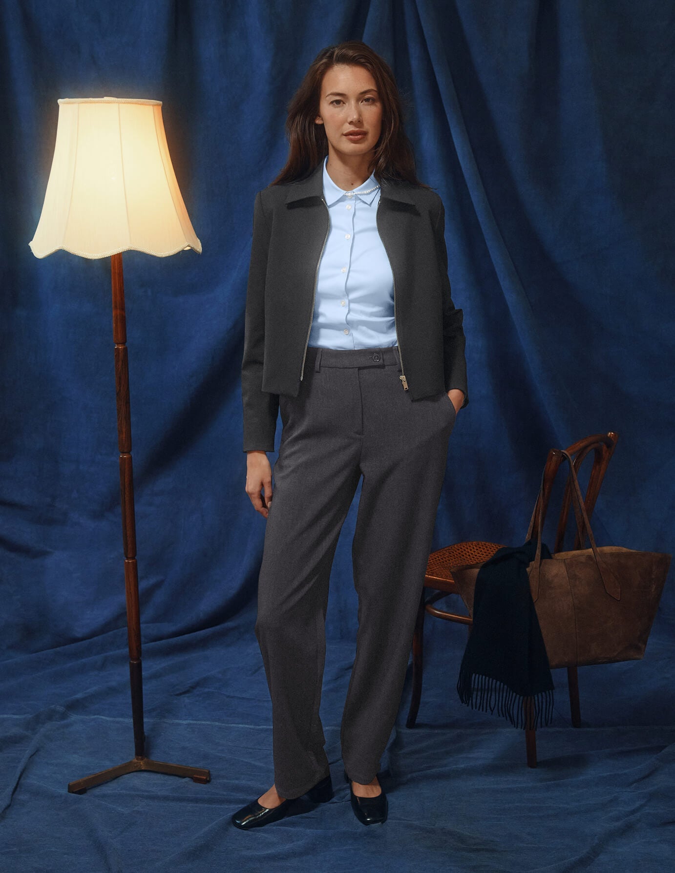 A woman wearing a dark grey melange Essential Short Zip Jacket over a light blue collared shirt and matching trousers.